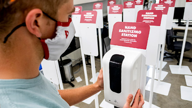 Image shows student working on hand sanitizer station in Rose-Hulman Ventures with completed stations lined up nearby.