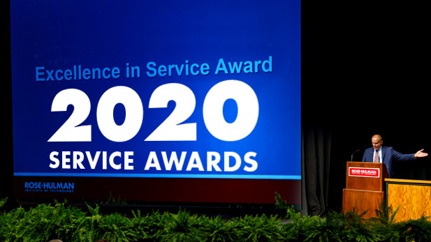 President Rob Coons on stage of Hatfield Hall with 2020 Service Awards displayed in large letters on the screen behind him.