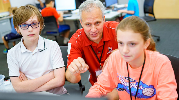 Two students smiling and working at a computer with Dr. David Fisher.