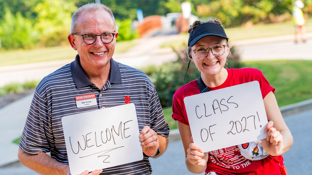 Rob Coons and Courtney Valmore hold up signs welcoming students to campus.