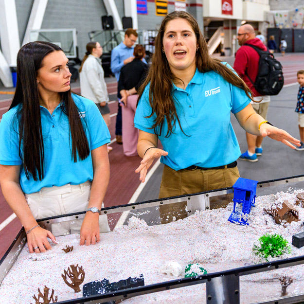 Two female team members explaining their project at the stream table.