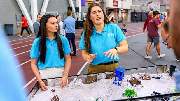 Two female team members explaining their project at the stream table.
