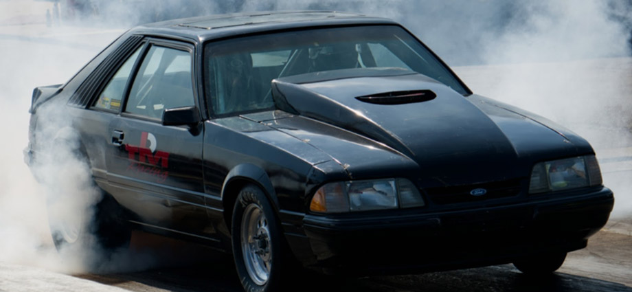 A black car zooms through a cloud of smoke.