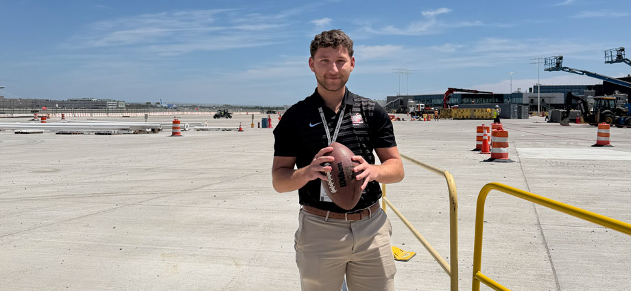 Andrew Mrozinske on an airport tarmac holding a football.