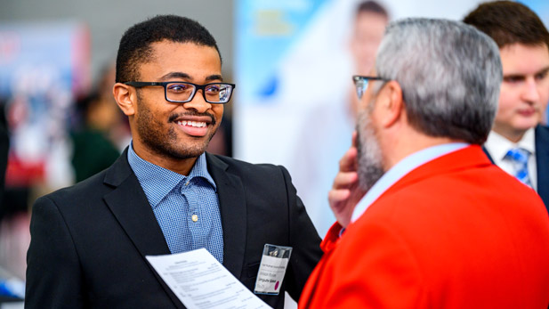 A smiling male student greets an employer at the Career Fair.