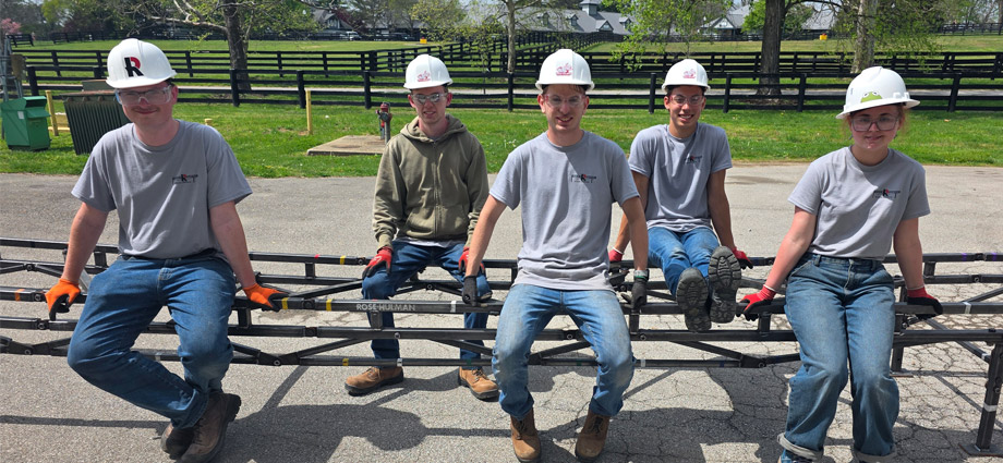Five students wearing hard hats and perch on their steel bridge project.