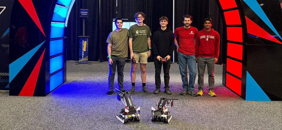 Five students with their two robots under an arch lit with red and blue LEDs.