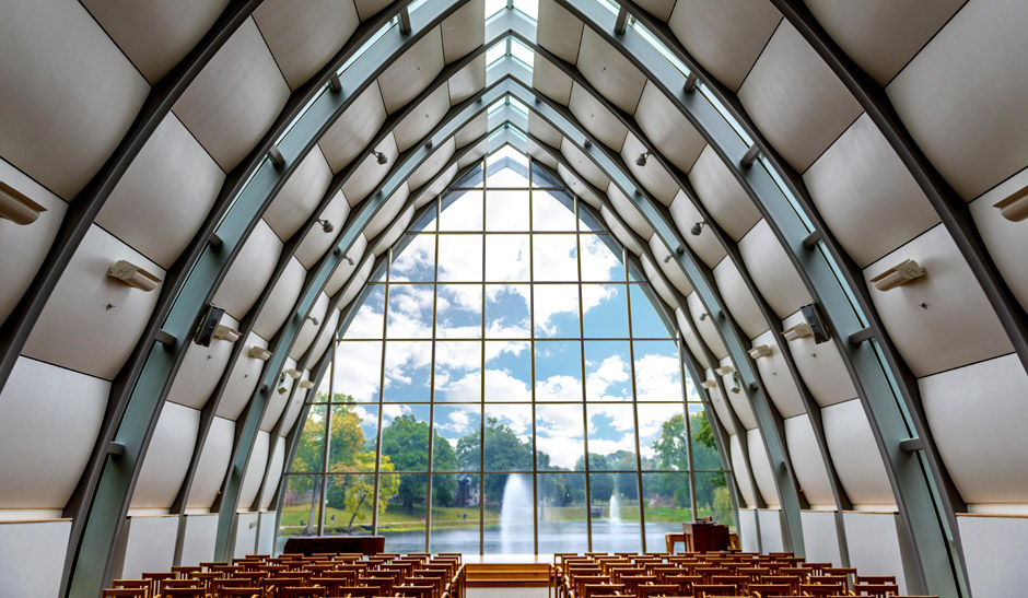 Interior view of White Chapel with Speed Lake visible through the windows of the chapel. Two lake fountains are operating in the distance spewing water high in the air.
