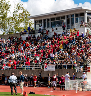 Image shows fans, many wearing Rose-Hulman red, filling the stands of Cook Stadium during a sunny afternoon