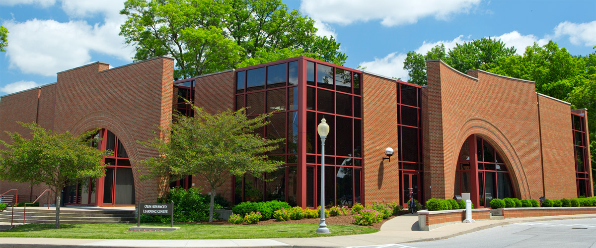 External view of New Olin Hall with green trees and a blue sky overhead. 